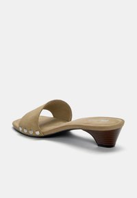 Bruine su�ède muiltjes met open teen en kruisband. Heeft decoratieve zilveren studs langs de zijkant en een gecontourde houten hak.