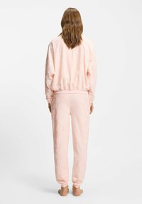 Chándal de color rosa claro con un diseño texturizado y el logo "Hugo", puños elásticos y pantalones deportivos a juego con un corte holgado.