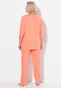 Korallfärgad loungewear-set med en topp med medellång ärm och byxor med prikar, tillverkade av mjukt, lätt tyg.