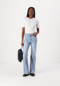 Jeans svasati azzurri chiari con vita alta; abbinati a una t-shirt bianca a coste. Scarpe nere e una borsa blu scuro completano il look.