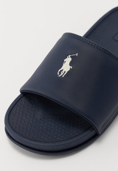 Sándalo azul marino hecho de material sintético texturizado. Presenta un diseño de punta abierta y un logo bordado en blanco de un jugador de polo.