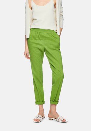 Woman wearing lime green rolled-up pants, white sleeveless top, cream cardigan slipping off shoulders, and white open-toe low-heeled sandals.