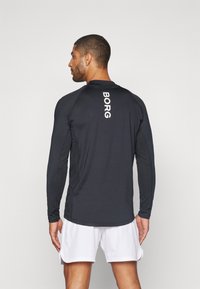 Juoda ilgomis rankovėmis sportinė marškinė, ant nugaros užrašytas žodis „BORG“ baltomis raidėmis. Audinys atrodo lygus ir prigludęs, derinamas su baltomis šortais.