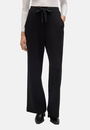 Pantalones de pierna ancha negros con una textura suave, con cintura ajustable y bolsillos laterales. Combinados con una blusa ajustada de manga larga y zapatos negros.