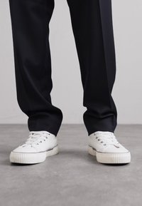 Hvide sneakers med en tekstureret gummisål, med snørebånd og metaløjer, parret med mørke, strømlinede bukser.