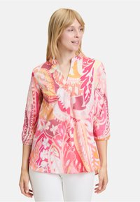 Blouse imprimée colorée avec un col à encoches, des manches trois-quarts et une coupe décontractée, fabriquée en tissu léger, avec des motifs roses et oranges.