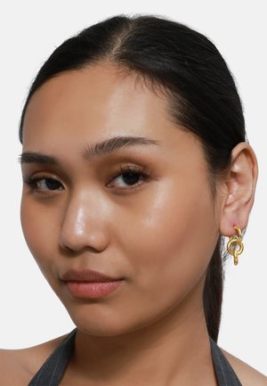 Boucles d'oreilles dorées avec des boucles entrelacées, dotées d'une finition polie. Le design présente une forme moderne et épurée avec une texture métallique.