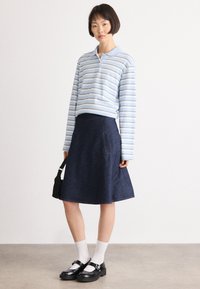 Stripete langermet polo skjorte i lys blå og hvit; kombinert med en mørk denim A-linje skjørt med sidelommer. Svarte sko og hvite sokker.