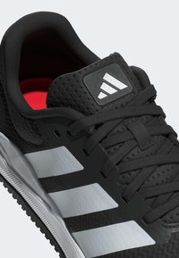 Botté de sport noir avec une tige texturée, intérieur rouge, rayures blanches sur le côté et un patch de logo sur la languette. Semelle en caoutchouc avec une bonne adhérence.