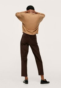 Brauner gerippter Pullover mit weit geschnittenem Schnitt, kombiniert mit dunkelbraunen Cordhosen. Schwarze Slipper werden getragen.