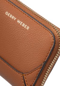 Cartera de cuero marrón con un acabado texturizado, con un zipper dorado y el logo en relieve "GERRY WEBER" en la parte frontal.