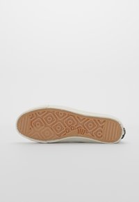 Vit sneakersula med hexagonala och cirkulära mönster i ljusbrunt. Texturerad gummi ger grepp. Förstärkt häl med en diskret logotyp.