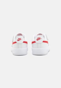 Valged Nike'i tenniseds punaste aktsentidega, mis on valmistatud siledast sünteetilisest materjalist, pehme kaelusega ja tekstureeritud tallaga, tagades hea haarde.