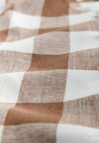 Detailní záběr na pomačkanou látku se vzorem hnědých a bílých kostiček.