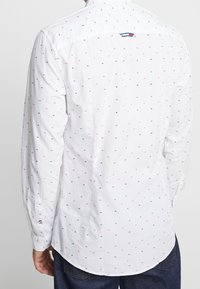 Camicia bianca con bottoni, caratterizzata da pois multicolori, maniche lunghe e orlo curvo. Realizzata in cotone leggero per garantire comfort.
