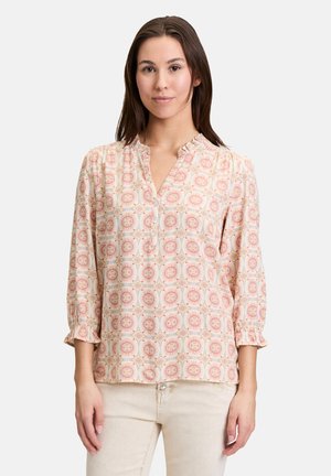 Blouse légère à manches longues en rose avec un motif géométrique, dotée d'un col en V et de poignets volantés. Tissu doux, coupe décontractée.