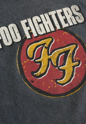 Graues Stoff-T-Shirt mit einem abgenutzten, kreisförmigen roten und gelben Grafikdesign, das den Text "Foo Fighters" und ein stilisiertes, ineinander verschlungenes Logo zeigt.