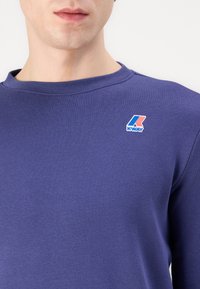 Paarse sweatshirt van zacht materiaal met een ronde halslijn en geribde manchetten. Bevat een klein blauw, rood en wit K-way logo op de borst.