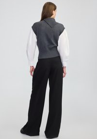 Grijze gebreide vest met een brede kraag, gedragen over een witte blouse, in combinatie met losse zwarte broeken. Soepele textuur, getailleerd ontwerp.