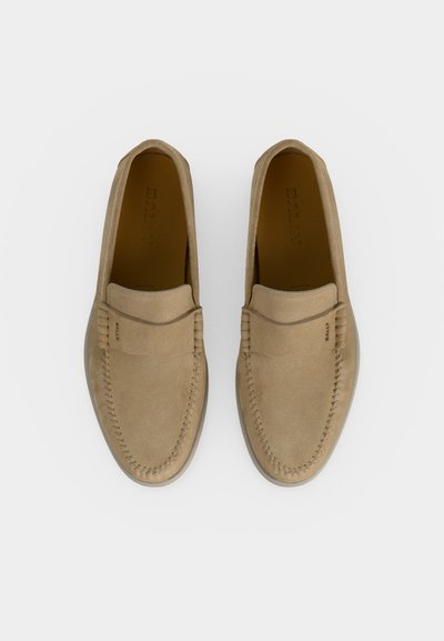 Ζευγάρι μπεζ δερμάτινα μοκασίνια με ραφή μοκασίνου και λεπτομέρεια με λουράκι, σε λευκό φόντο, από πάνω.