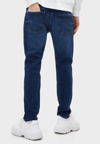 Mörkblå denimjeans med smal passform, utrustade med en klassisk design med fem fickor och subtila vita sömmar. Kombinerade med robusta vita sneakers.