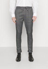 Grå rutiga byxor med dragsko i midjan, avsmalnande design och slät yta. Kombineras med svarta dressade skor.
