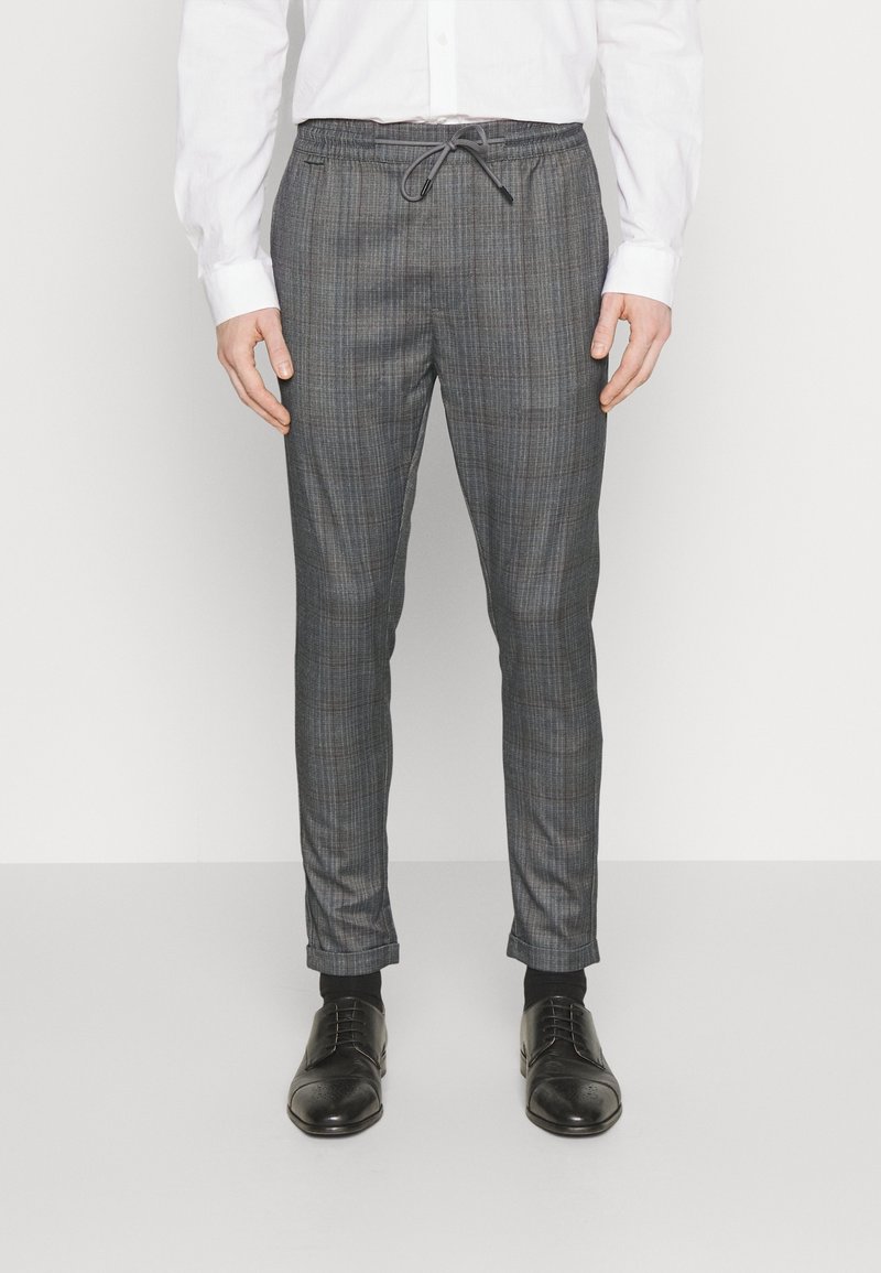 Grå rutiga byxor med dragsko i midjan, avsmalnande design och slät yta. Kombineras med svarta dressade skor.