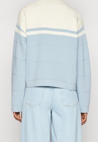 Jasnoniebieska krótka bluza z białymi i jasnoniebieskimi poziomymi paskami, wykonana z miękkiego materiału; w zestawie z jasnoniebieskimi dżinsami.