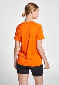 Orange tränings t-shirt med korta ärmar, med rund hals och vita detaljer på axlarna. Slät, lättviktsmaterial.