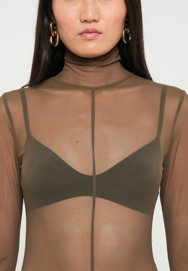 Transparante bruine mesh coltrui met lange mouwen, met daaronder een donkergroene driehoekige bralette en een verticale naad in het midden.