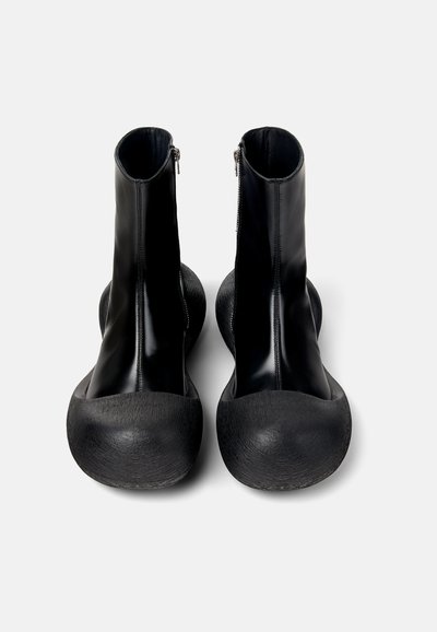Svarta ankelstövlar med en glänsande finish, med dragkedjestängning, rund tå och texturerad gummisula. Släta och hållbara material.