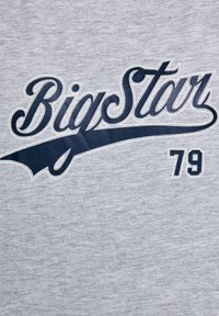 Hall kriitline T-särk, millel on sinise kaldkiri tekst "Big Star", mida täiendavad kumer riba ja number "79" kastikujuliseks fondiks.