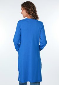 Blaue langärmlige Tunika aus strukturiertem Stoff, mit Rundhalsausschnitt, seitlichen Schlitzen und lässiger Passform. Geeignet für legere Kombinationen mit Jeans.