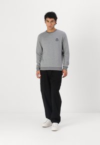 Sudor deten gri dintr-un amestec de bumbac, cu guler rotund și logo brodat. Asortat cu pantaloni negri și adidași albi. Design simplu și casual.