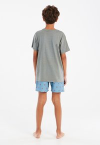 Camiseta gris de manga corta combinada con pantalones cortos azules con un patrón de palmeras. El conjunto tiene un ajuste casual y holgado y está hecho de una tela suave.