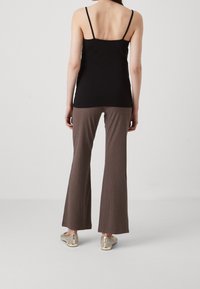 Svart spaghetti band topp, bruna ribbade flare byxor och guldprydda skor. Slät textur och åtsittande siluett.