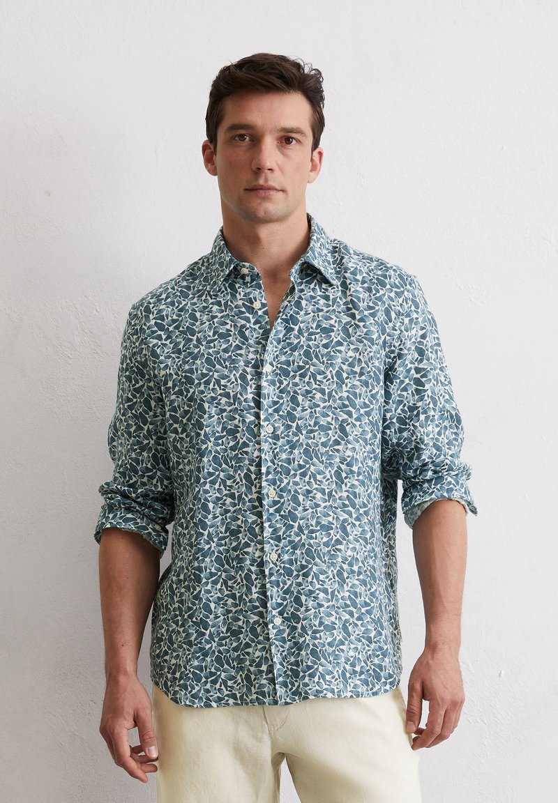 Chemise boutonnée de couleur bleu clair avec un motif de feuilles blanches. Manches longues retroussées, tissu doux, poche plaquée unique sur le côté gauche de la poitrine.
