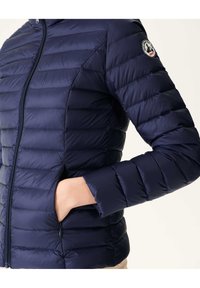 Marine blauwe pufferjack met horizontale stiksels, een rits aan de voorkant en zijzakken. Glad, glanzend materiaal met een getailleerde pasvorm. Logo op de mouw.