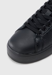 Sneaker in pelle nera con suola spessa, lacci neri e dettagli in rilievo a forma di stella e lettere sul pannello laterale.