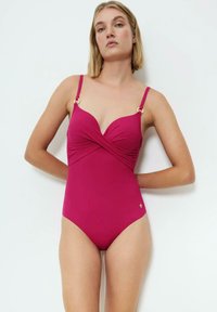 Bañador de una pieza en fucsia con tirantes ajustables, diseño frontal retorcido y detalles en tono dorado. Textura suave, forma ceñida.