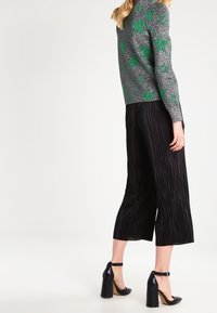 Pull gris avec motif d'étoiles vertes, associé à un pantalon culotte plissé noir et des chaussures à talons bloc noires et brillantes. Design simple, sans logos notables.