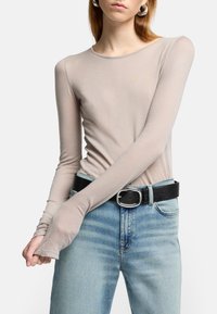 Lys beige langærmet top lavet af et blødt materiale, med rund halsudskæring og tætsiddende design, parret med højtaljede blå jeans og et sort bælte.