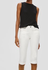 Mustat hihattomat tekstuuripaidat yhdistettynä valkoisiin lyhyisiin farkkuihin, joissa on käännetyt hihansuut ja perinteinen viisi-taskuinen muotoilu.