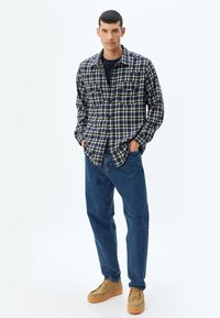 Havsblå och vit rutigt flanellskjorta med två bröstfickor, tillsammans med blå jeans och bruna loafers, mot en enkel bakgrund.