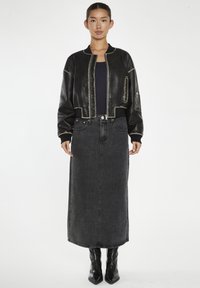 Giacca bomber in pelle nera con cuciture a contrasto, abbinata a una lunga gonna di jeans nera e stivaletti neri lucidi.