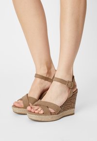 Braune Keilsandalen mit strukturiertem Absatz, verstellbarem Knöchelriemen und Überkreuzband-Design; aus Wildleder und Jute gefertigt.