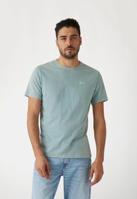 Camiseta de algodón azul claro con cuello redondo y mangas cortas. Presenta un logo sutil en el pecho y un acabado suave y texturizado.