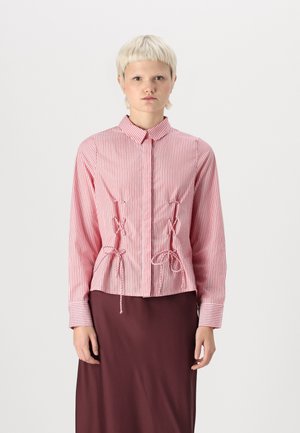 Chemise à boutons rayée rouge et blanche avec des manches longues, dotée d'une taille ajustée avec des liens et d'un col classique. Tissu en coton lisse.