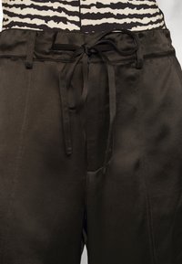 Svarta satinbyxor med knytmidja, med en mjuk struktur och två sidofickor. Tyget har en lätt lyster och faller elegant.