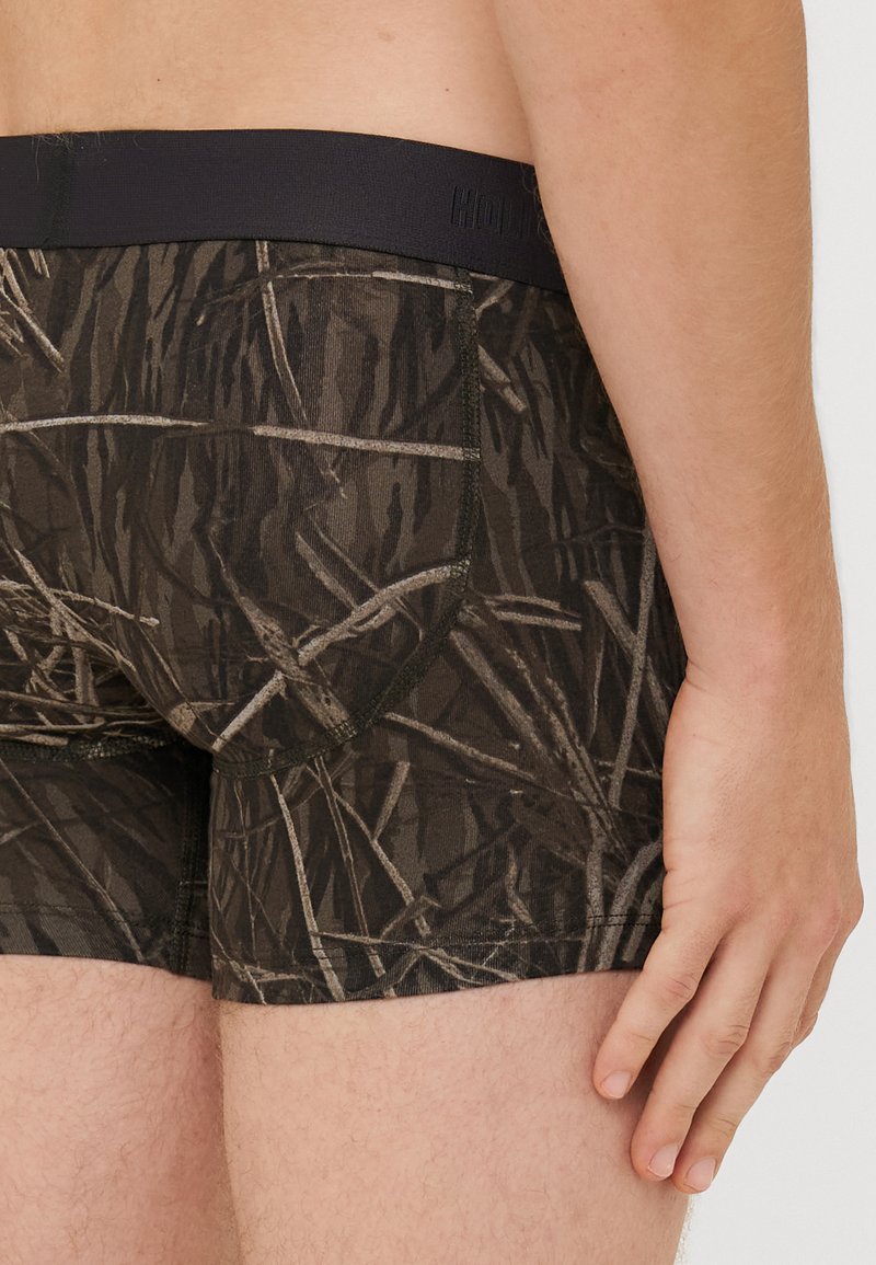 Męskie slipy w ciemnym wzorze kamuflażu, z czarnym elastycznym pasem, wykonane z miękkiego i rozciągliwego materiału.